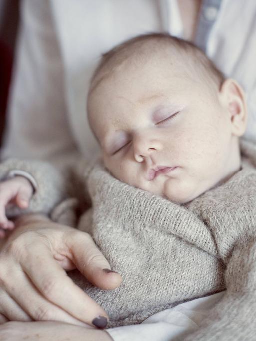Ein neugeborenes Baby schläft auf dem Schoß seiner Mutter.
