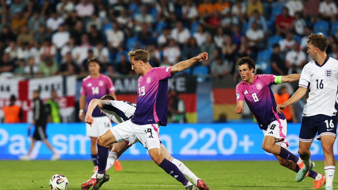 Drei deutsche Fußballer in pinken Trikots und zwei englische Fußballer in weißen Trikots kämpfen um den Ball. 