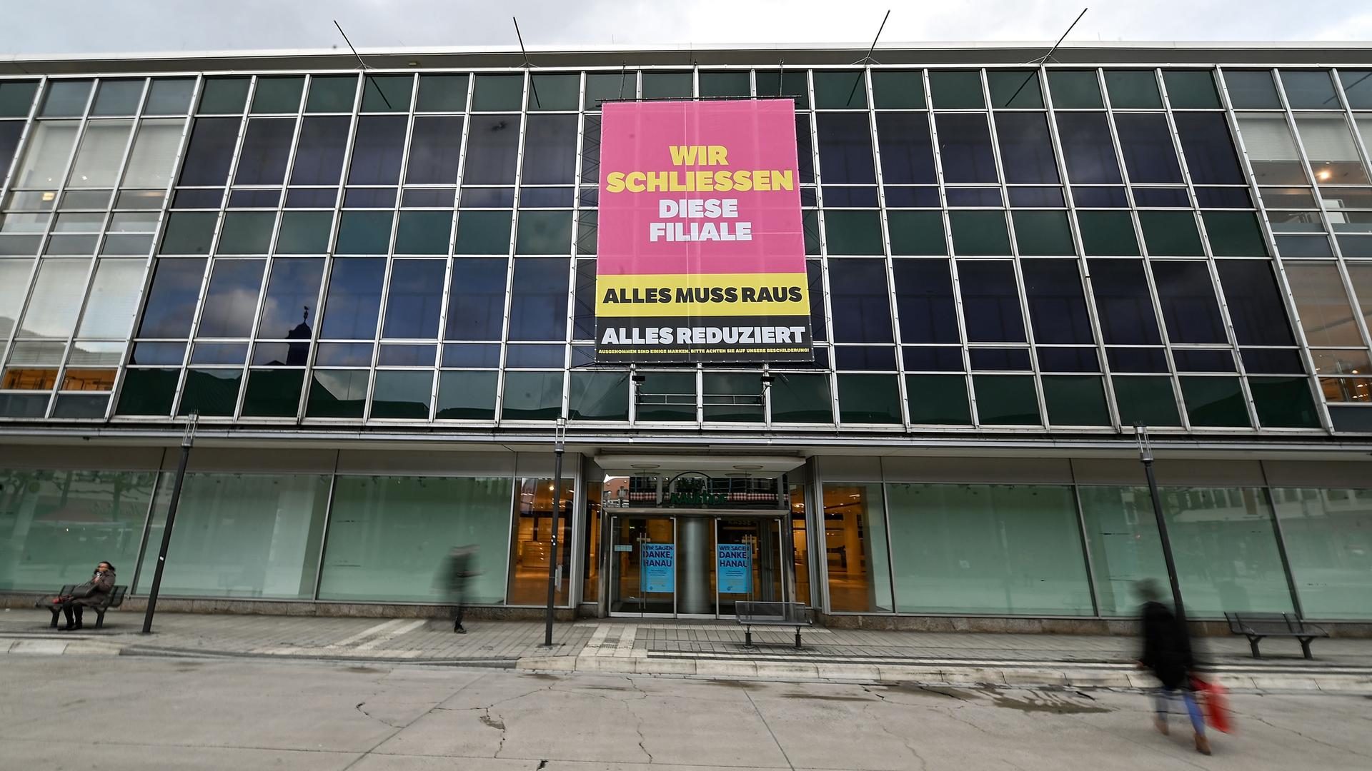 An einem Kaufhaus ist ein Transparent mit der Aufschrift "Wir schließen diese Filiale" angebracht. 