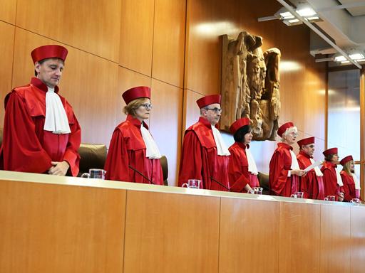 Stehende Männer und Frauen in roten Roben.