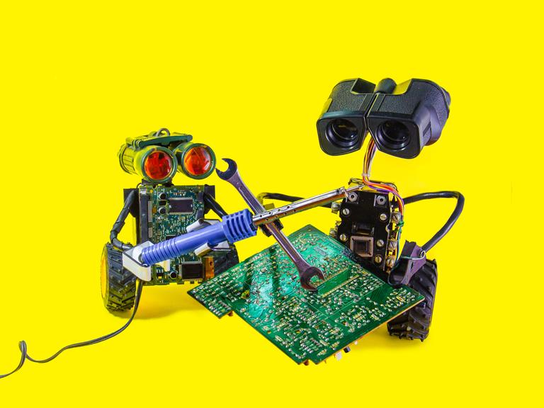 Zwei fröhliche spielzeugartige Roboter reparieren eine Leiterplatte mit Lötkolben vor knallgelbem Hintergrund. 