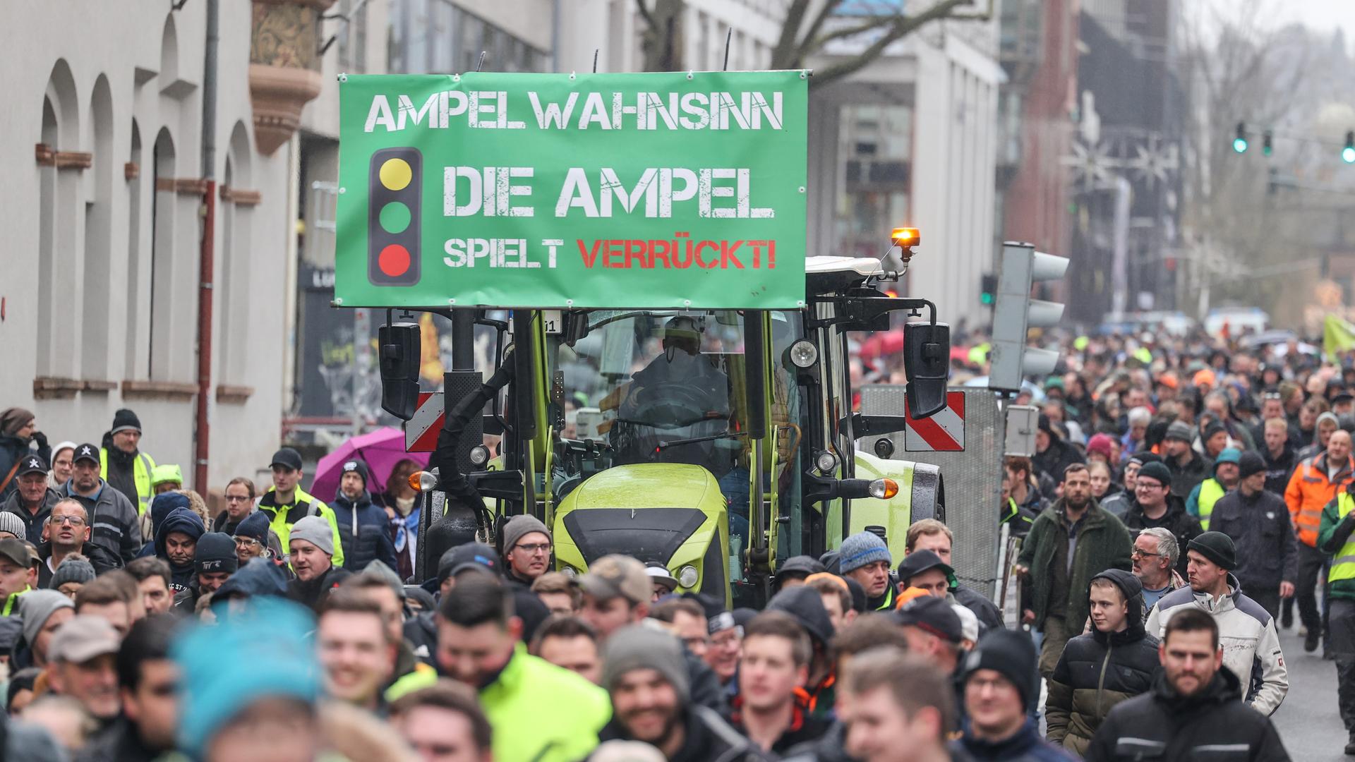 Teilnehmer einer Protestaktion gehen neben einem Traktor, an dem ein Schild mit der Aufschrift "Ampel-Wahnsinn - die Ampel spielt verrückt!" angebracht ist. 
